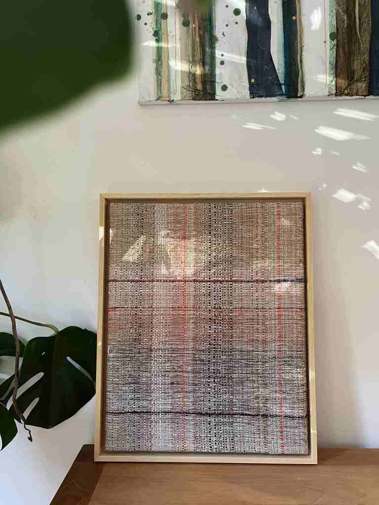 Woven framed art panel shown with monstera plant