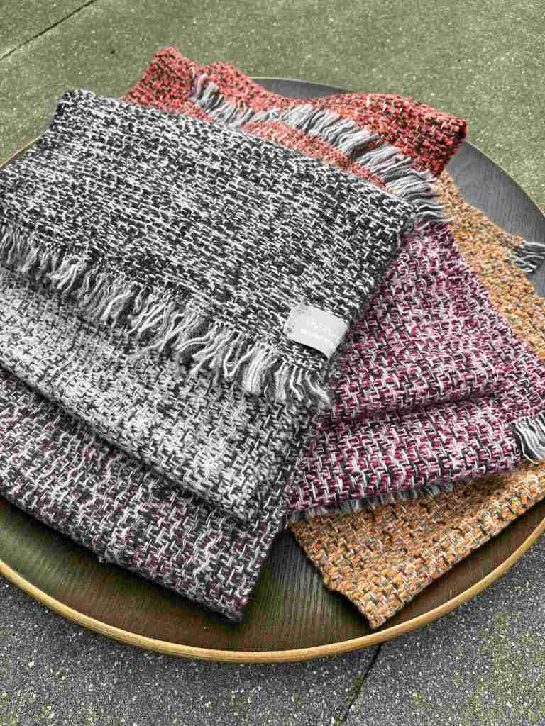 A collection of handwoven scarves in various colors, neatly arranged on a round wooden plate.