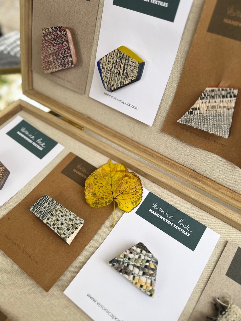 Display of handmade textile brooches on cardboard backing with a yellow autumn leaf.