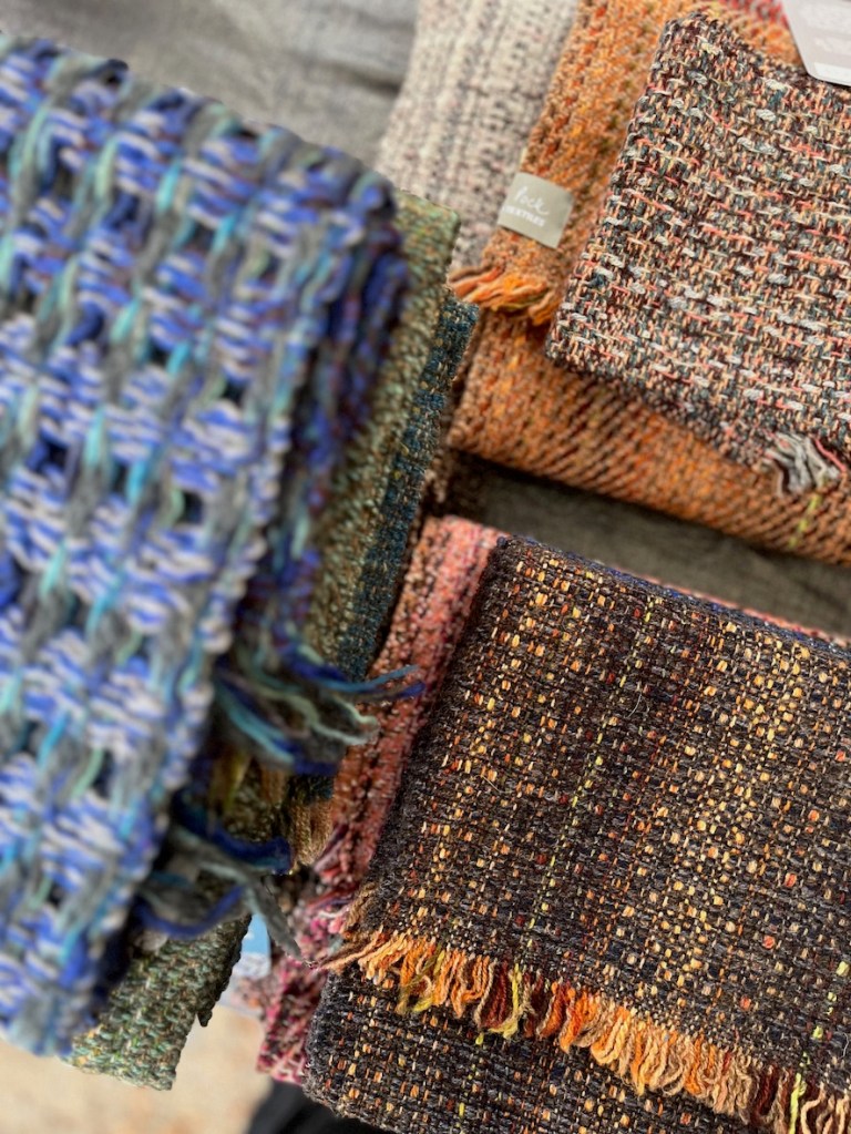 A close-up of woven textiles displaying a variety of colors and textures, including vibrant blues, earthy browns, and warm oranges, stacked together.