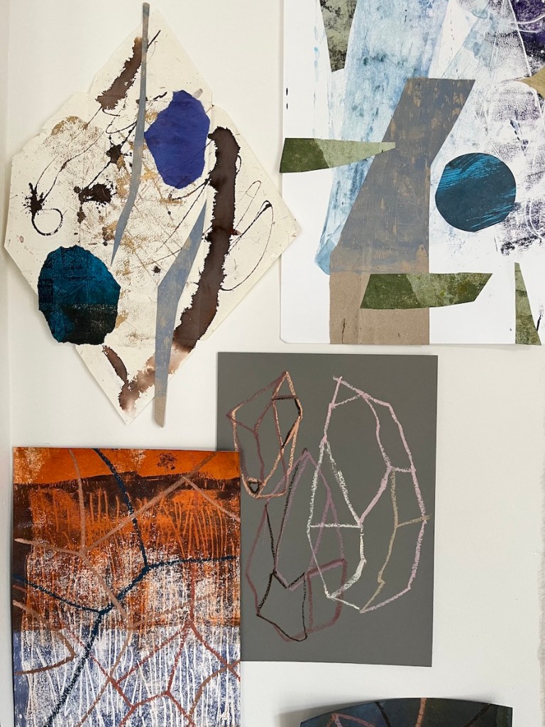 A collection of abstract artworks displayed on a wall, featuring various shapes and colors including blue, brown, black, and orange.