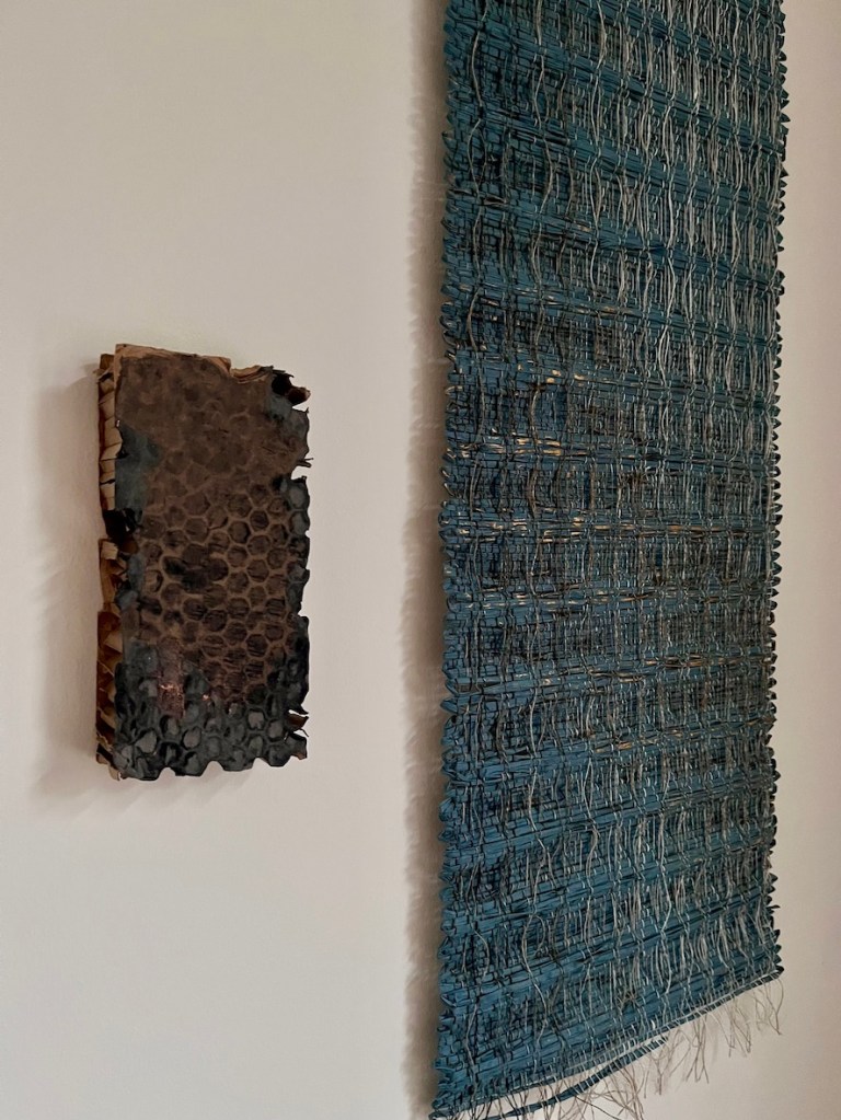 Artistic weaving displayed on a wall featuring a textured piece on the left and a larger woven wall hanging on the right.