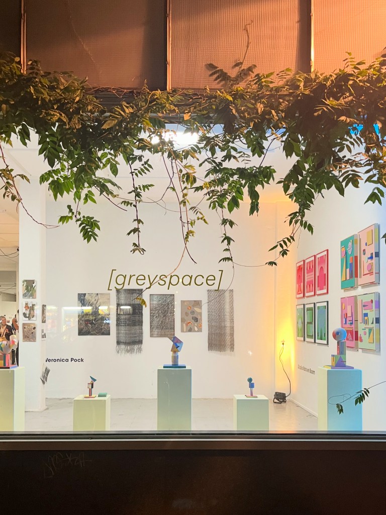 View of an art gallery named '[greyscape]', featuring assorted artworks by Veronica Pock, displayed on pedestals with a decorative vine framing the scene.